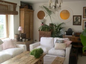 Salón luminoso con sofás blancos, plantas, ventanales circulares y madera